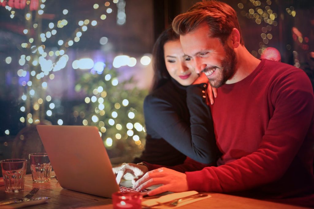 man-in-red-long-sleeved-shirt-853151 A couple using a laptop at a cozy restaurant with festive bokeh lights, enjoying online shopping together.
